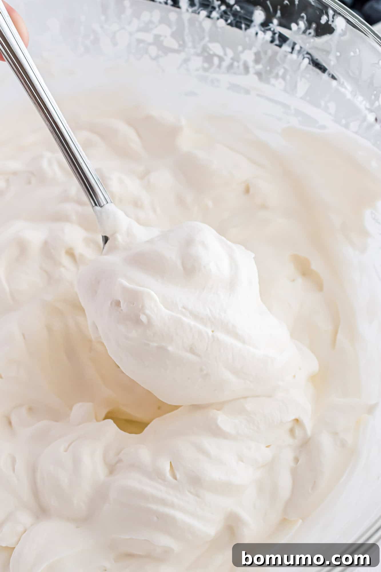 Freshly whipped cream, on a spoon, in a mixing bowl, showcasing its perfect texture.