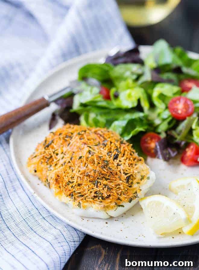 Crispy Parmesan baked cod served on a plate next to a vibrant green tossed salad, highlighting a healthy and delicious meal option.