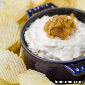 A dark blue bowl of creamy homemade French onion dip topped with caramelized onions, surrounded by ripple-cut potato chips.