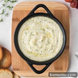 Overhead view of a small black pan filled with baked goat cheese dip, sprinkled with fresh thyme.