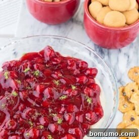 Bright red cherry cheesecake dip, garnished with lime zest, a vibrant holiday dessert.
