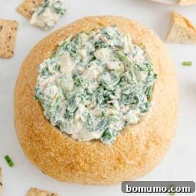 Creamy spinach dip served in a rustic bread bowl, ideal for holiday parties.