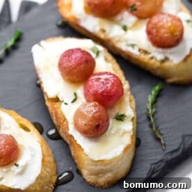 Image of roasted grape crostini arranged on a black slate board, topped with ricotta, roasted grapes, and honey.