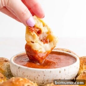 A stuffed pizza bite being dipped into marinara sauce, highlighting its cheesy interior.
