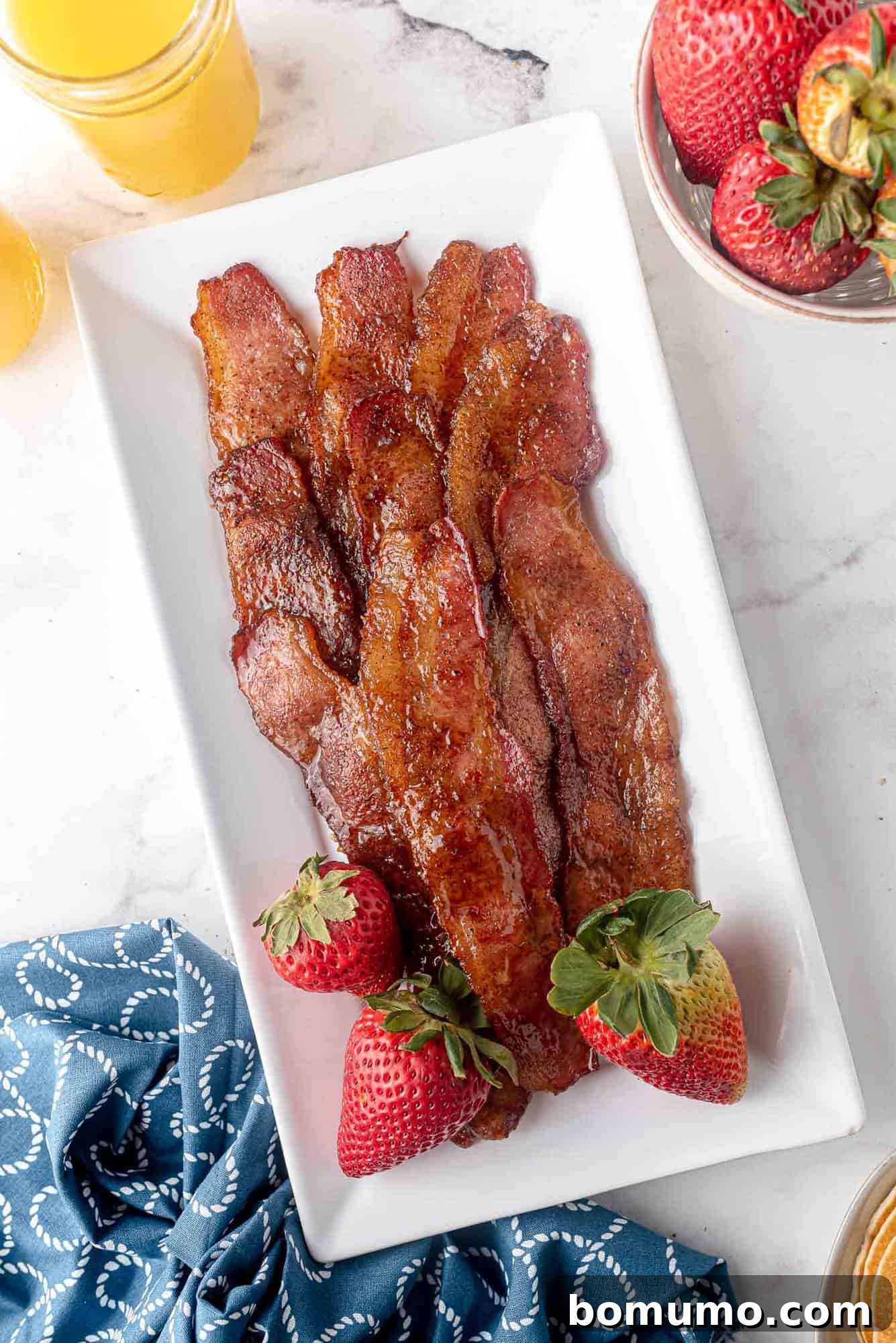 Crispy candied bacon served on a large platter with fresh strawberries, showcasing its enticing glaze.