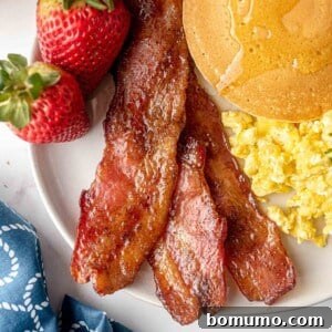 Candied bacon served on a plate with pancakes and eggs for a hearty breakfast.