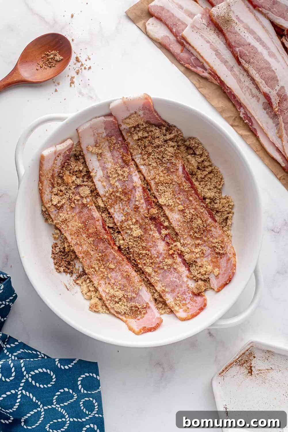 A thick-cut bacon slice being thoroughly coated by hand in the sweet and spicy seasoning blend.