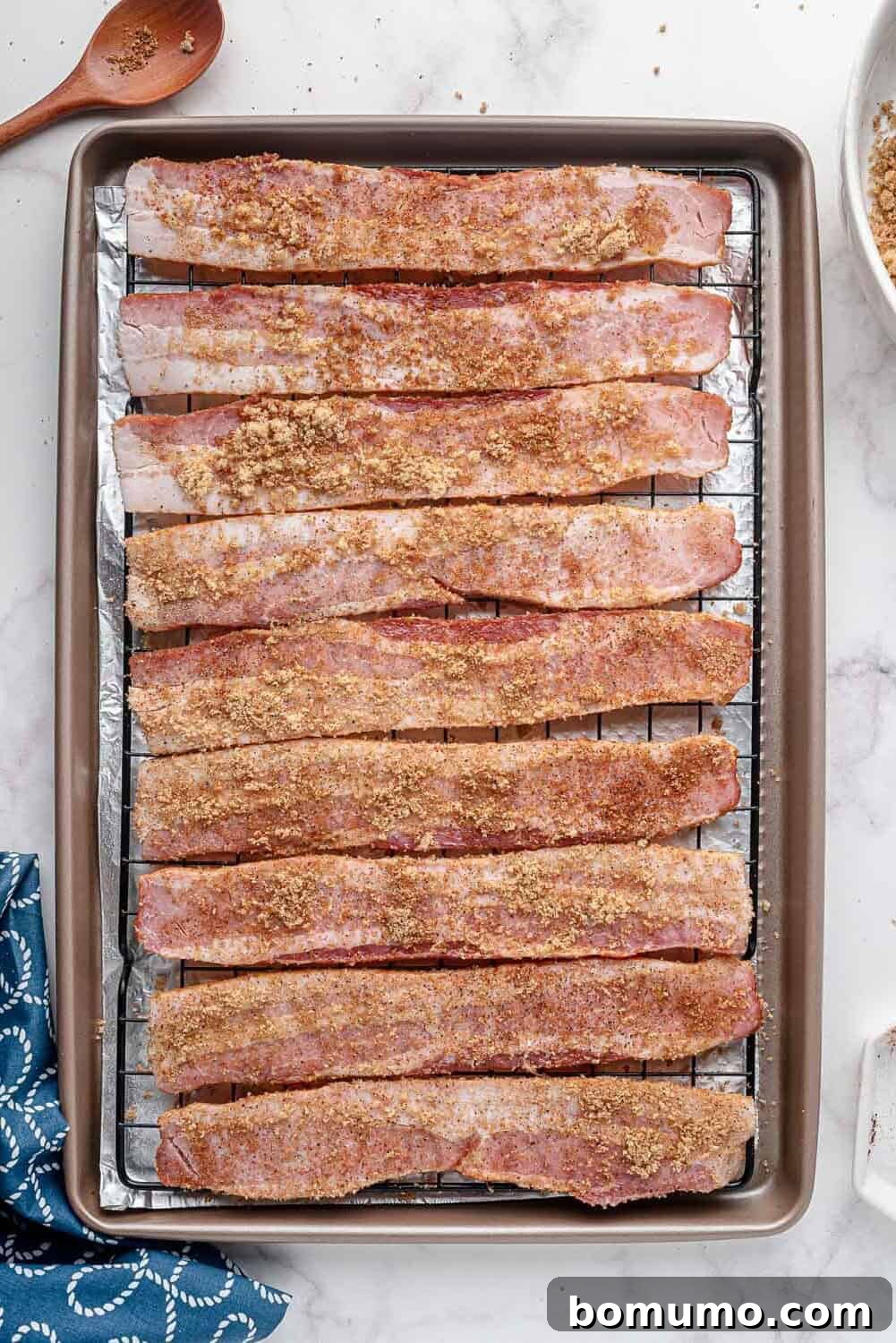 Rows of uncooked, spice-coated bacon strips neatly arranged on a wire rack, prepared for baking.
