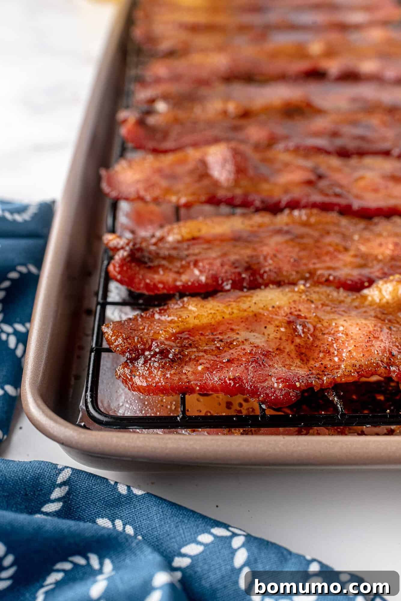 Crispy, glistening candied bacon strips cooling and further crisping on a wire rack.