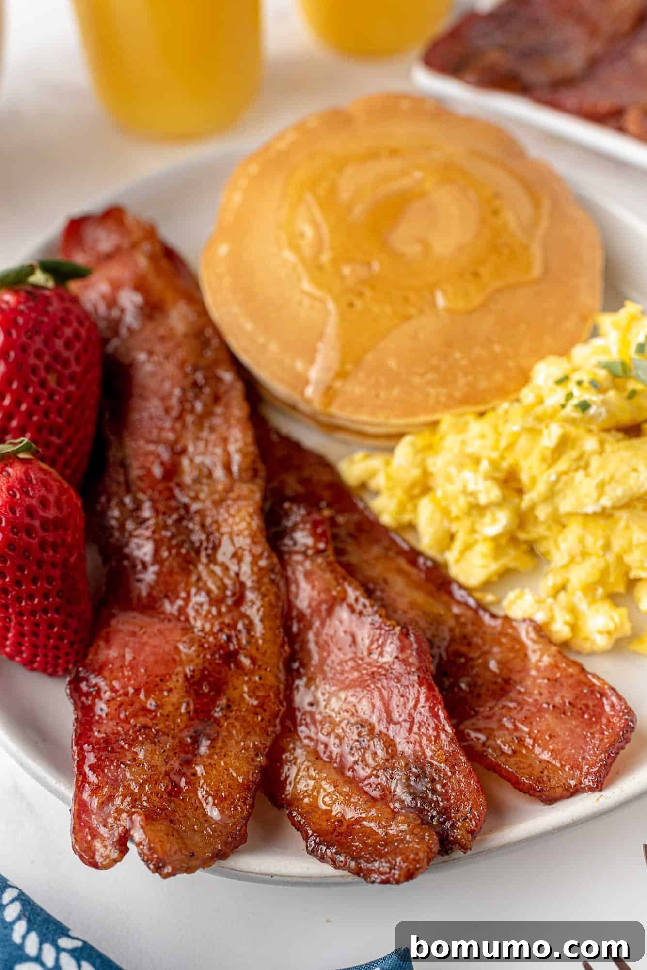 Candied bacon expertly plated alongside fluffy scrambled eggs and golden pancakes, forming a delicious and balanced breakfast.