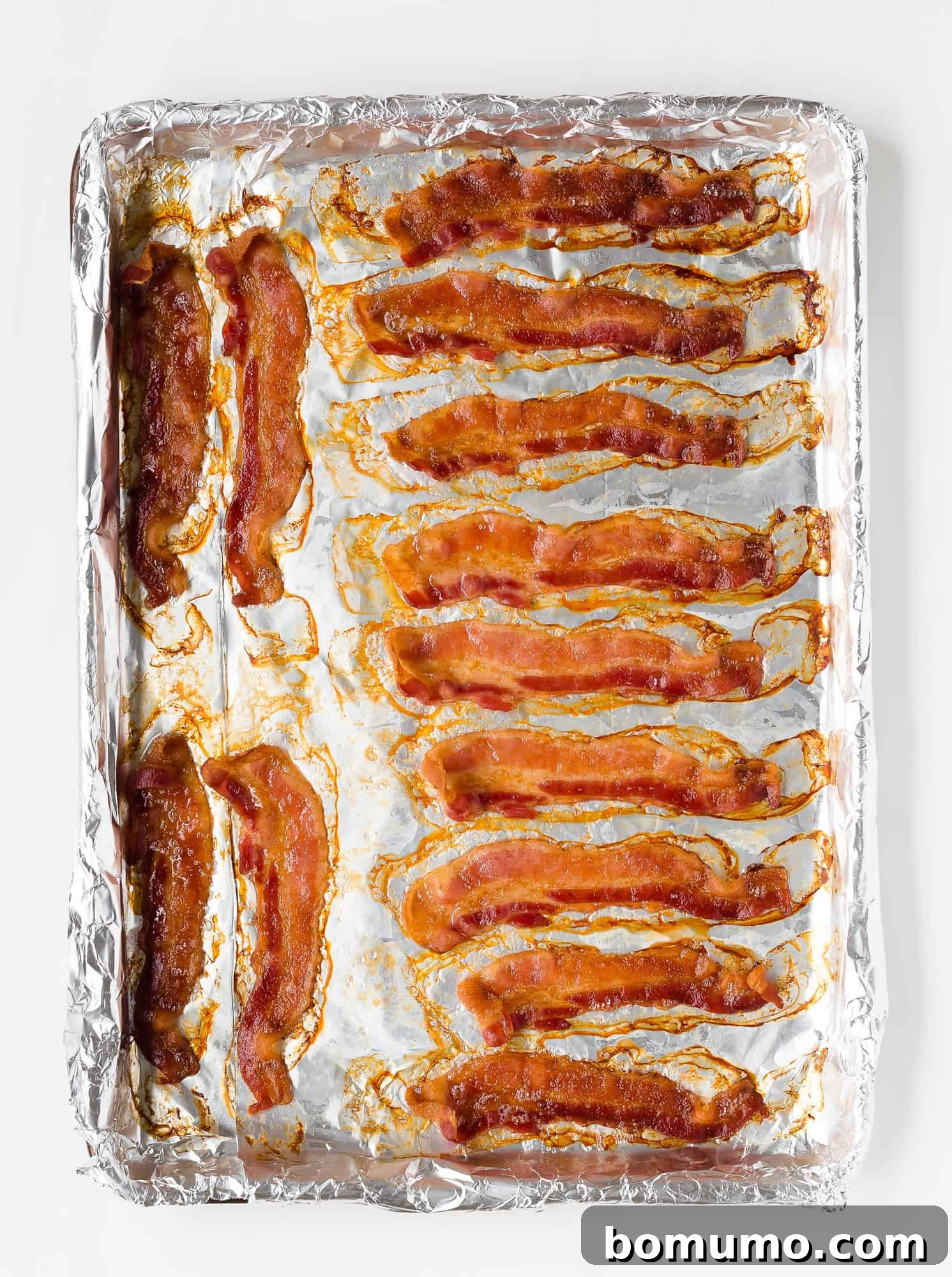 Perfectly cooked crispy bacon slices cooling on a foil-lined baking sheet, showing their golden-brown color and flat appearance.
