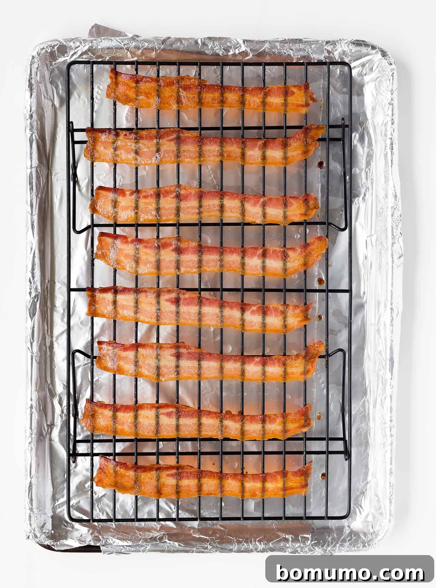Crispy baked bacon strips on a wire rack, allowing excess grease to drip into the pan below. Each strip appears perfectly straight and uniformly crisp.
