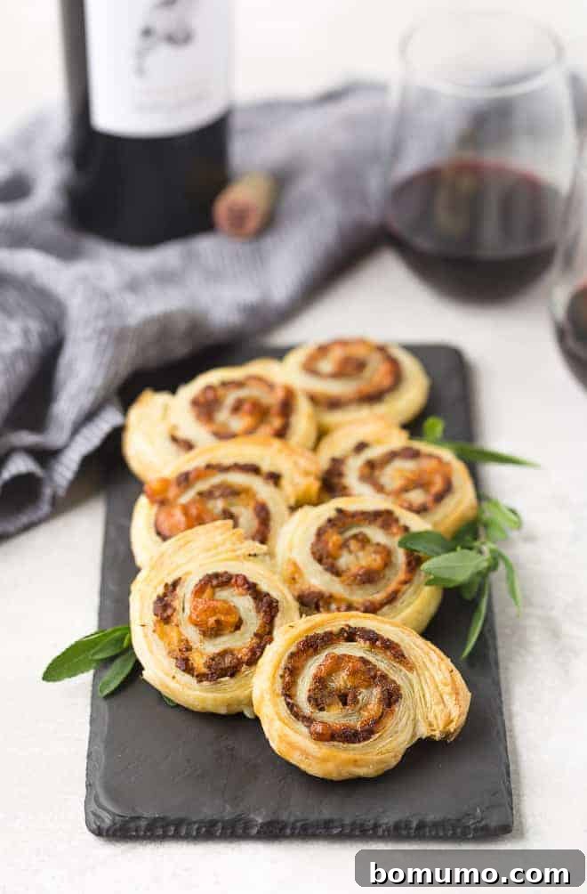Puff pastry pinwheels on a slate board with fresh sage. Red wine in background.