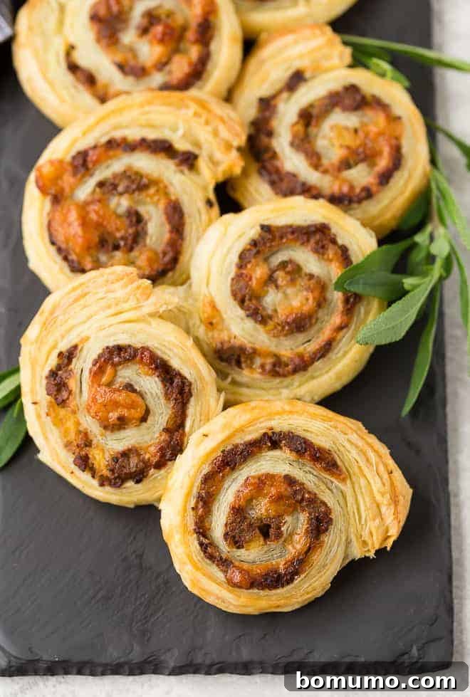 Pinwheels made with puff pastry, sausage, apple, cheese, and sage. Arranged on black slate.