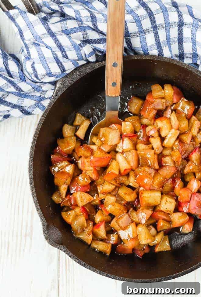 This apple compote recipe is an easy fruit topping bursting with the flavors of apples and spice. Add it to all of your fall recipes! Apple compote in a cast iron skillet, with a spoon.