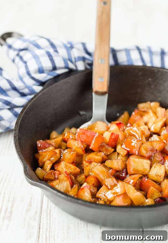 This apple compote recipe is an easy fruit topping bursting with the flavors of apples and spice. Add it to all of your fall recipes! Apple compote in a cast iron skillet, with a spoon.