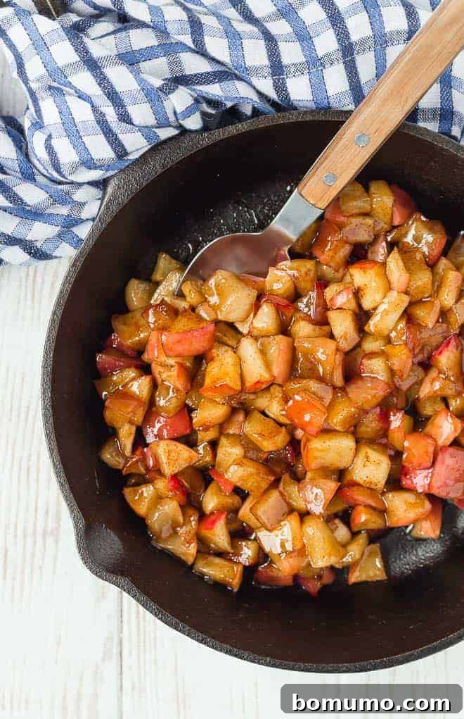 This apple compote recipe is an easy fruit topping bursting with the flavors of apples and spice. Add it to all of your fall recipes! Apple compote in a cast iron skillet, with a spoon.