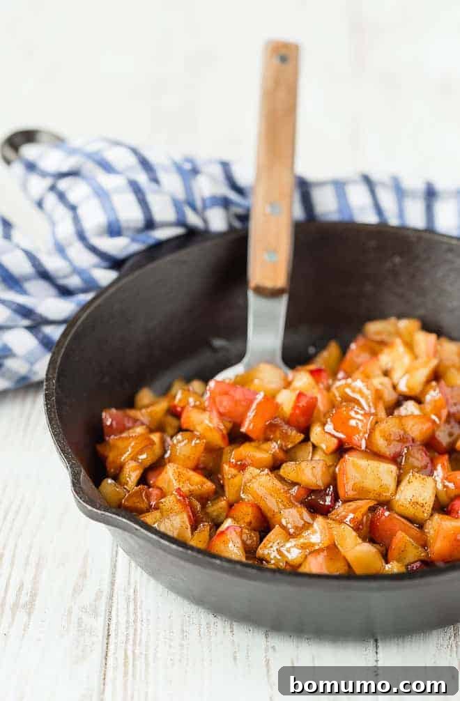 This apple compote recipe is an easy fruit topping bursting with the flavors of apples and spice. Add it to all of your fall recipes! Apple compote in a cast iron skillet, with a spoon.