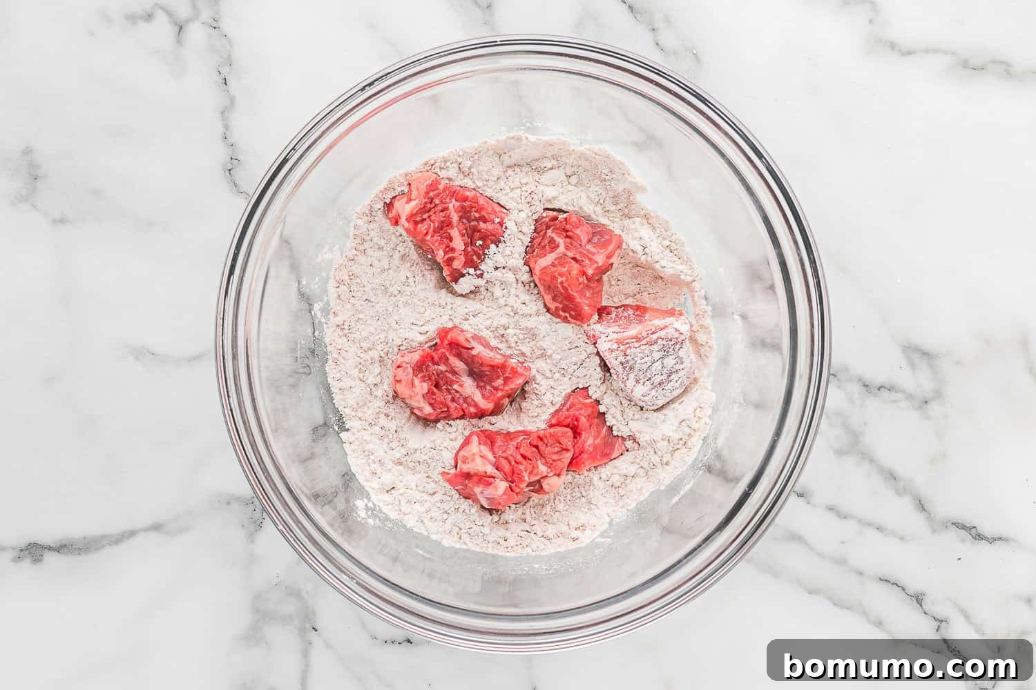 Beef cubes being tossed and coated in seasoned flour mixture in a bowl.