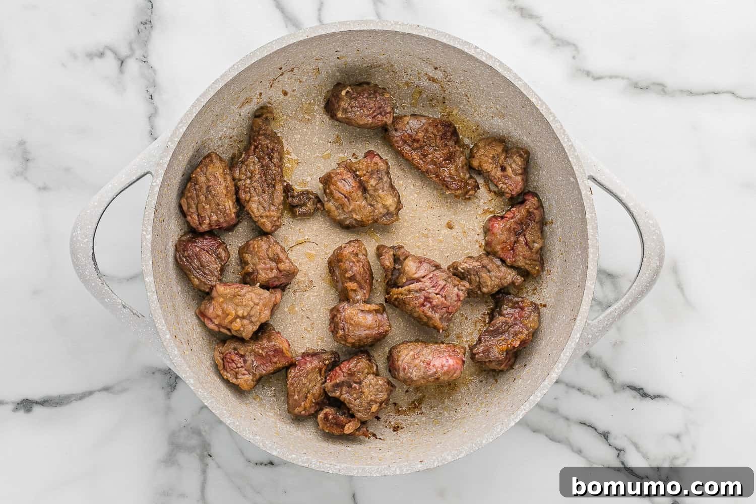 Beef cubes browning in a hot skillet, developing a rich crust.