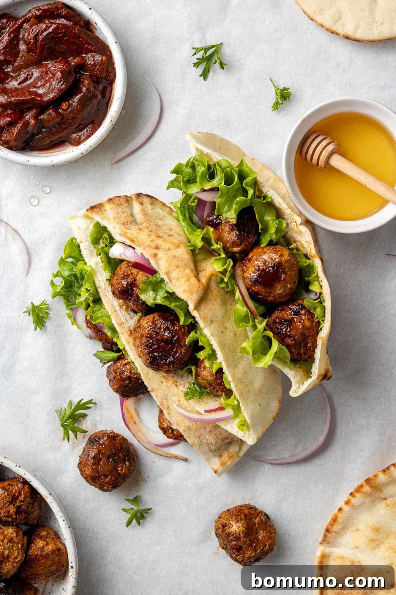 Overhead view of meatballs on a pita with lettuce, honey and chipotle chiles nearby.