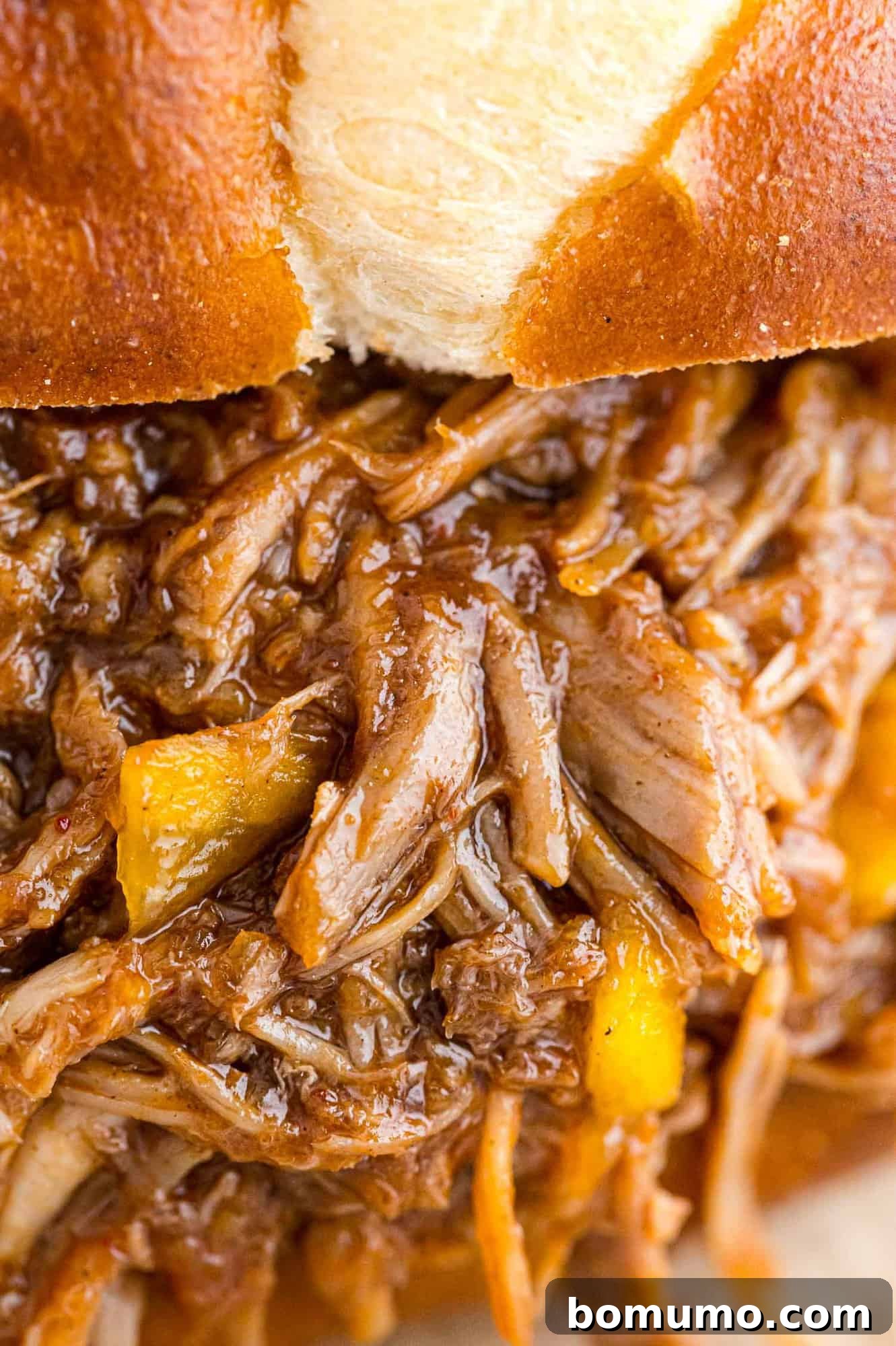 Very close up view of pulled pork with mango, on a bun.