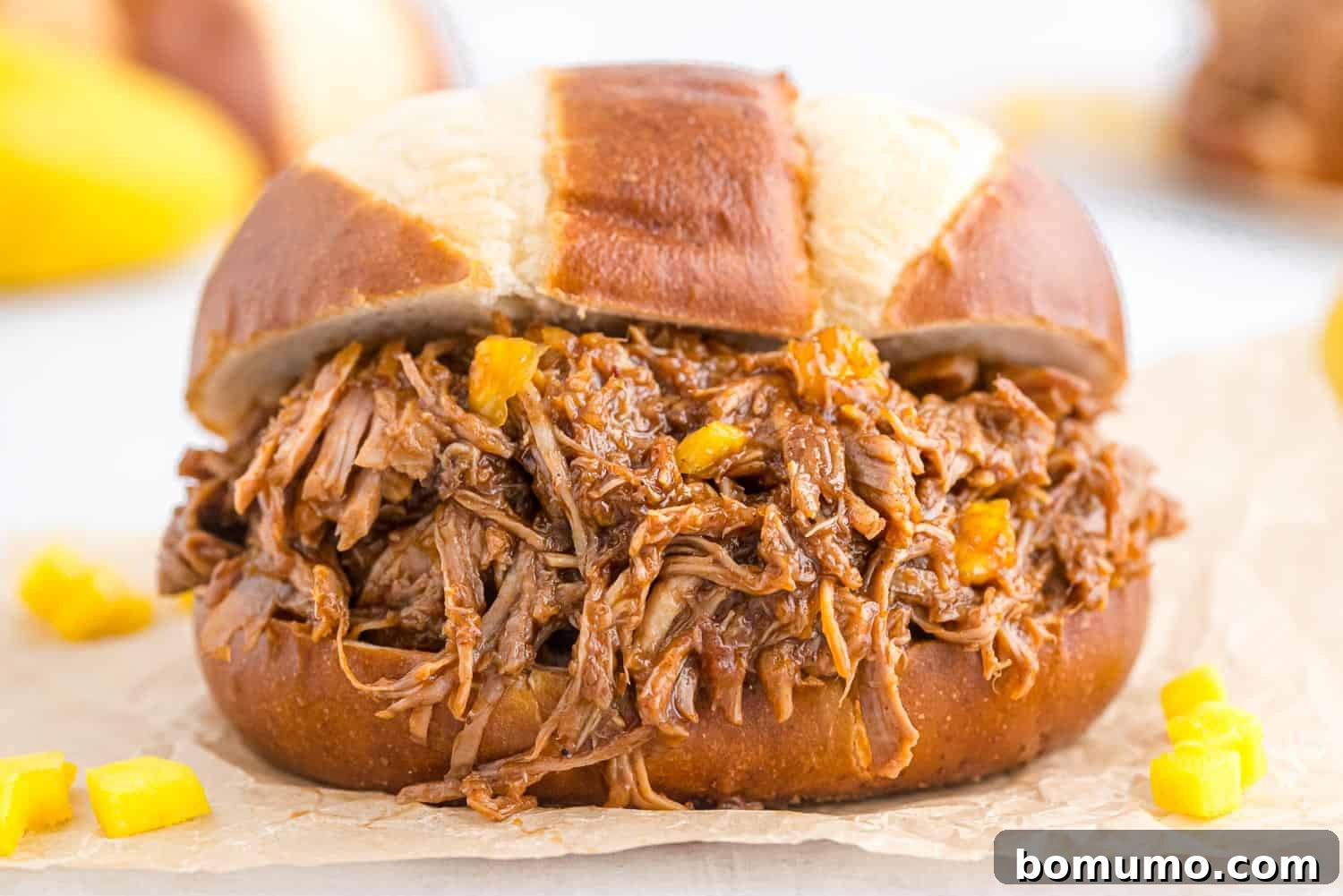 Pulled pork spilling out of a pretzel bun.