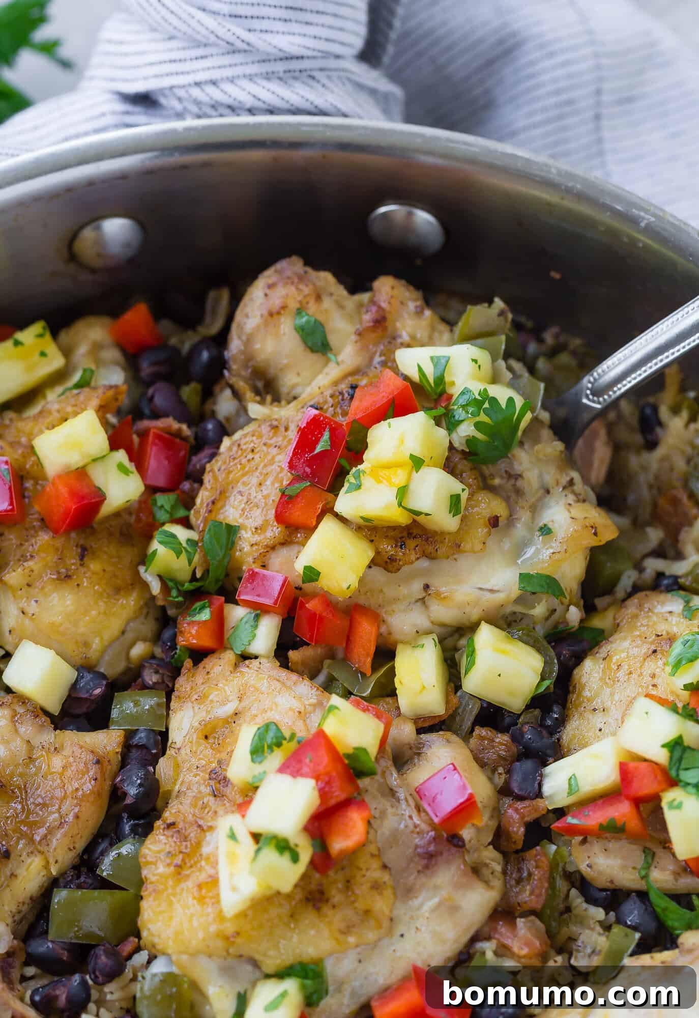 Cuban chicken thigh on a spoon in a pan, on a bed of rice.