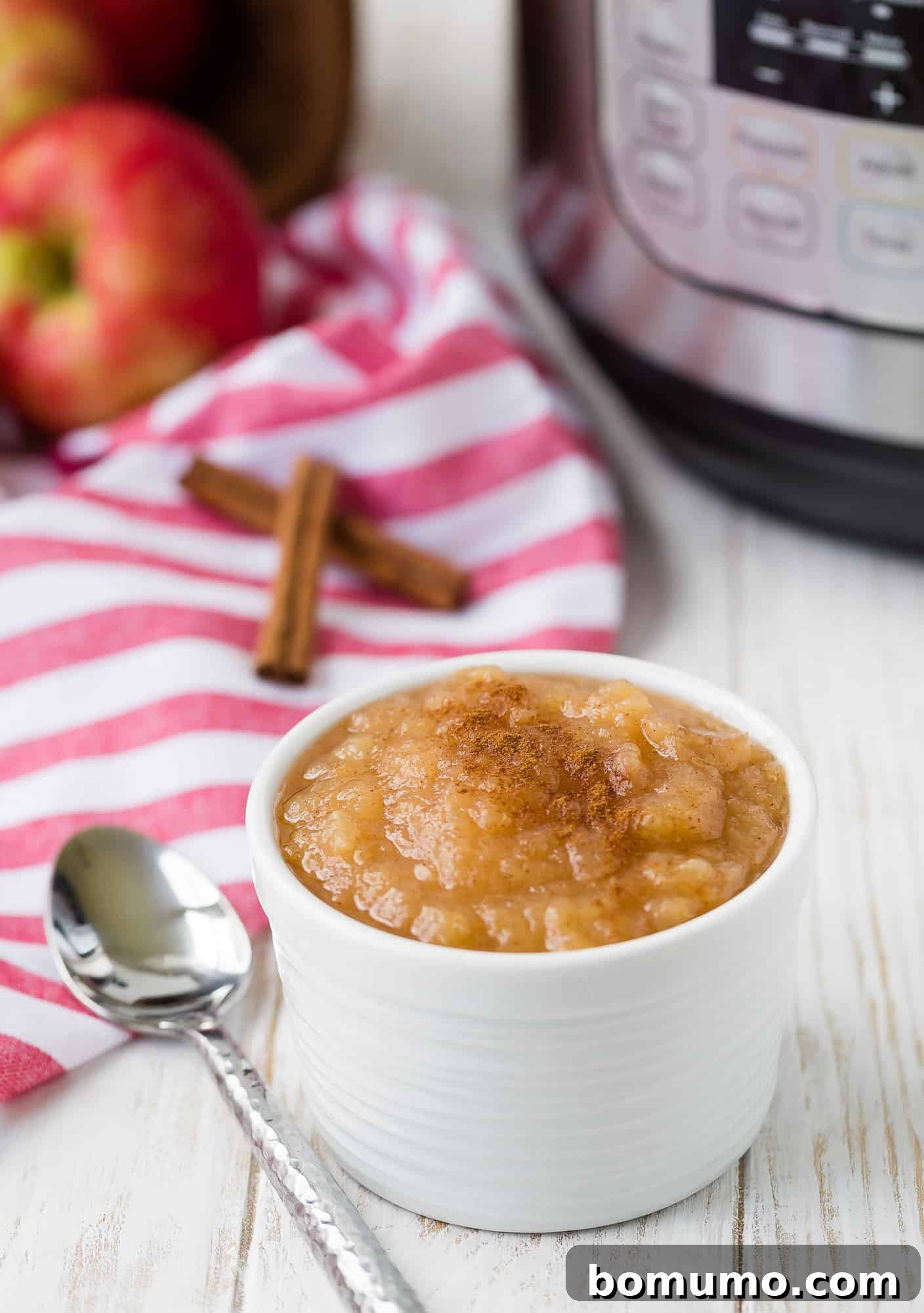 Simple Instant Pot Applesauce 6 Applesauce in a small white bowl with a spoon, Instant Pot in the blurred background.