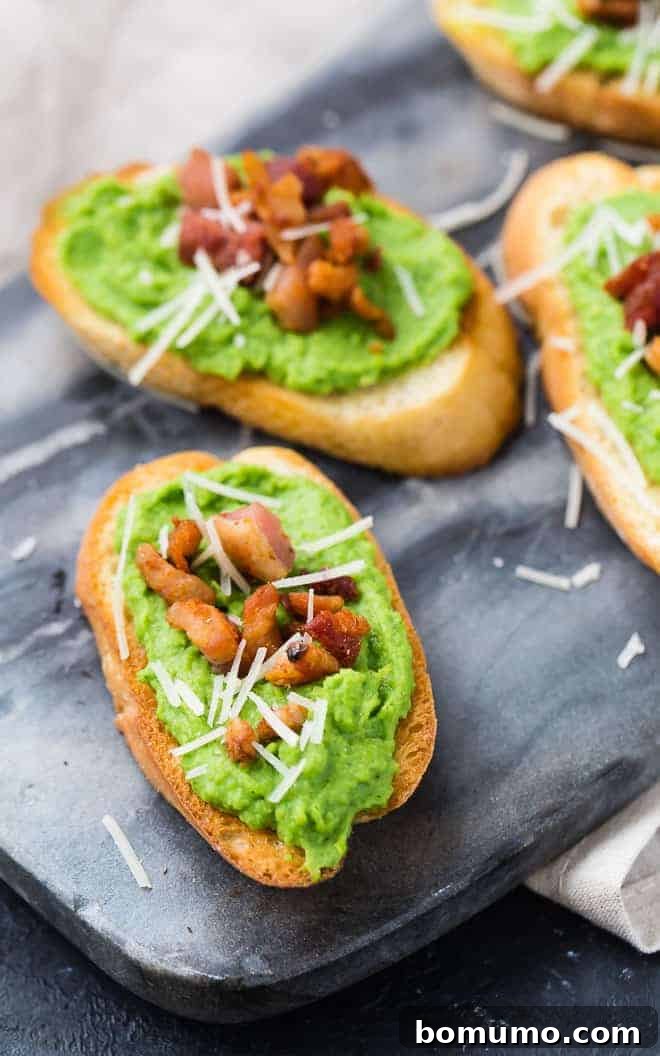 A striking image of vibrant green creamy pea crostini, artfully arranged on a black marble serving platter. Each crostini is generously topped with crispy pancetta bits and grated Parmesan cheese, highlighting the fresh mint and chive flecks in the pea puree.