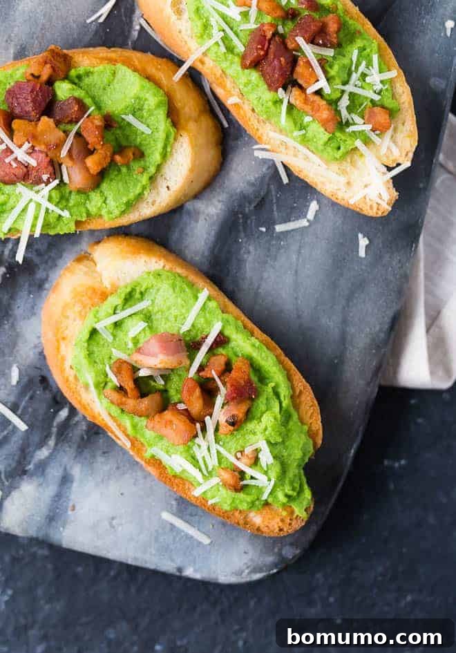 A perfectly plated creamy pea puree crostini, featuring a generous layer of vibrant green pea spread, topped with golden crispy pancetta and finely grated white Parmesan cheese, highlighting its elegant presentation.