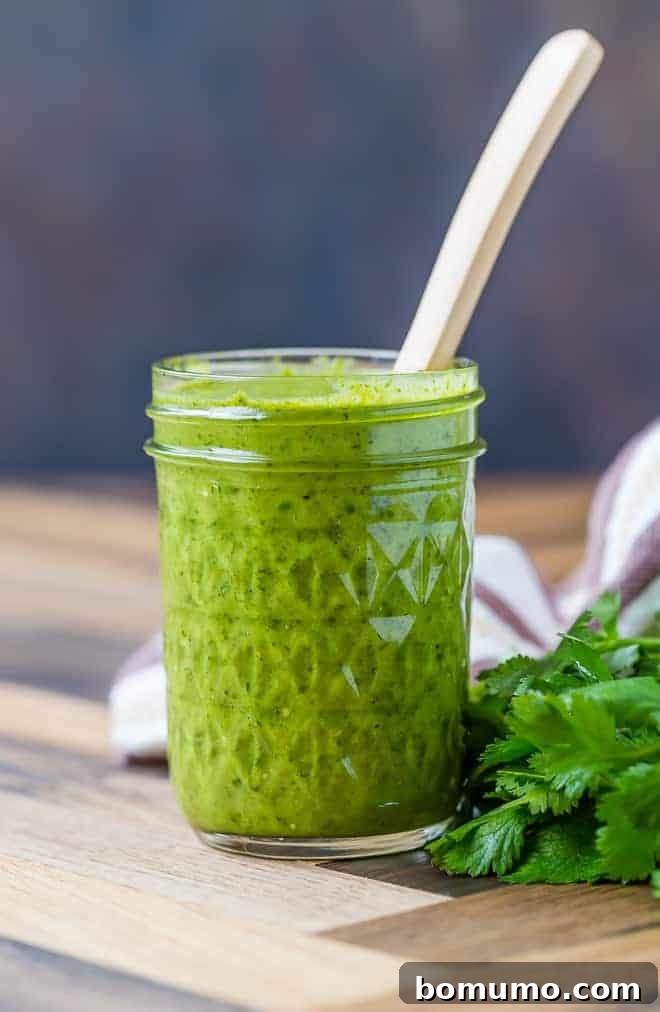 One-Pan Breakfast Tostadas 3 Image of freshly made salsa verde in a jar, with a spoon inserted, showcasing its vibrant green color and fresh texture.
