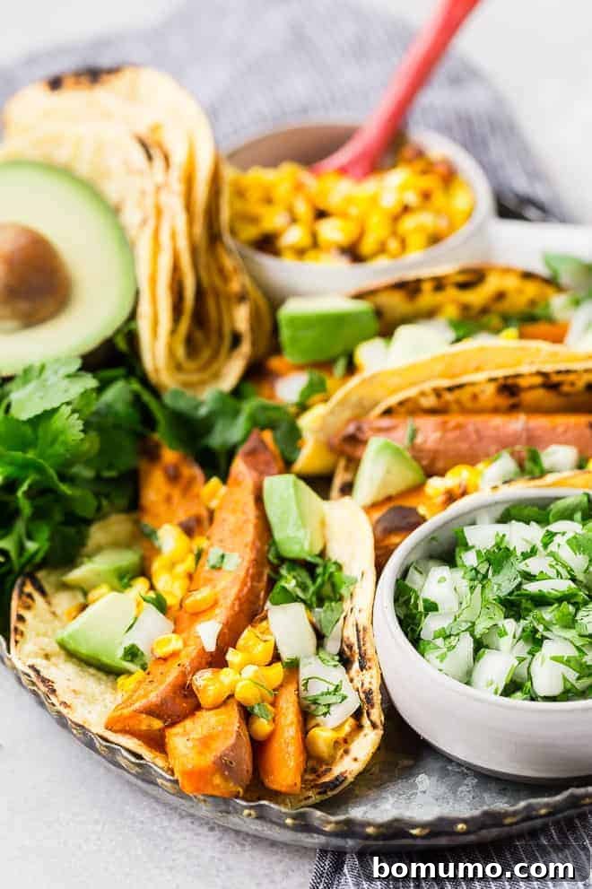 Close-up photograph of crispy sweet potato tacos on a wooden serving board, highlighting the beer-marinated roasted sweet potatoes, charred corn, creamy avocado, and fresh cilantro, embodying a true vegetarian taste sensation.