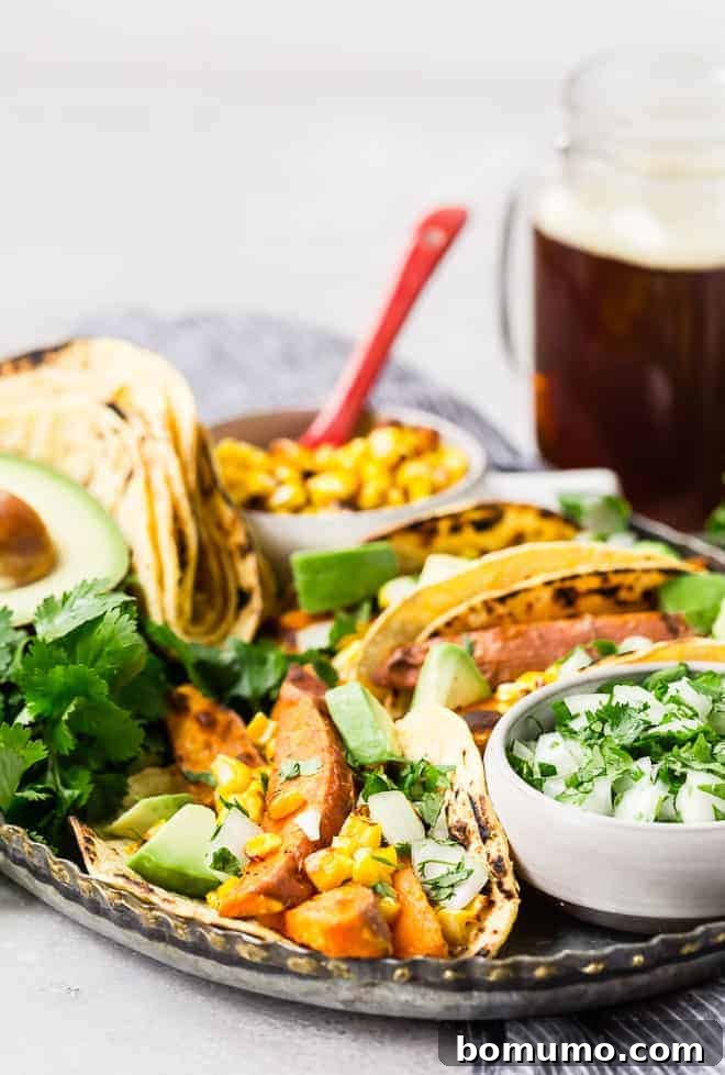 A close-up shot of a serving of delicious vegan tacos, prominently featuring the roasted sweet potatoes, fresh corn kernels, and perfectly sliced avocado.