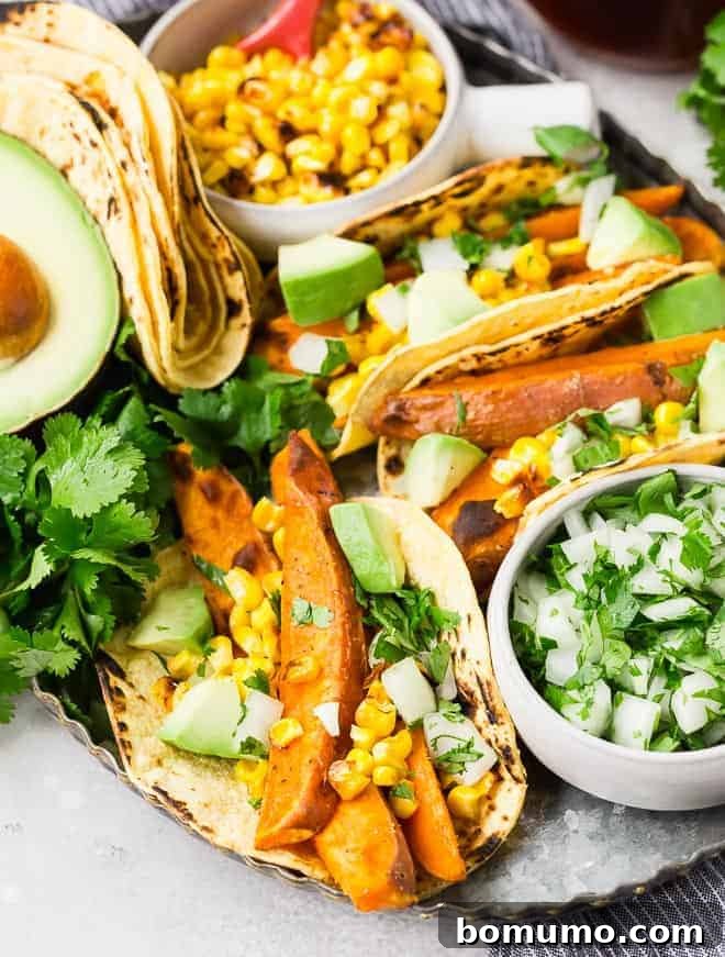 A vibrant platter featuring multiple delicious vegan sweet potato tacos, alongside an array of fresh toppings including corn, creamy avocado, and aromatic cilantro, ready for a delightful serving.