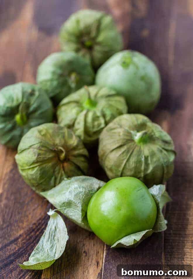 Image of fresh tomatillos on a rustic wooden surface, with one tomatillo partially peeled to reveal its vibrant green fruit.
