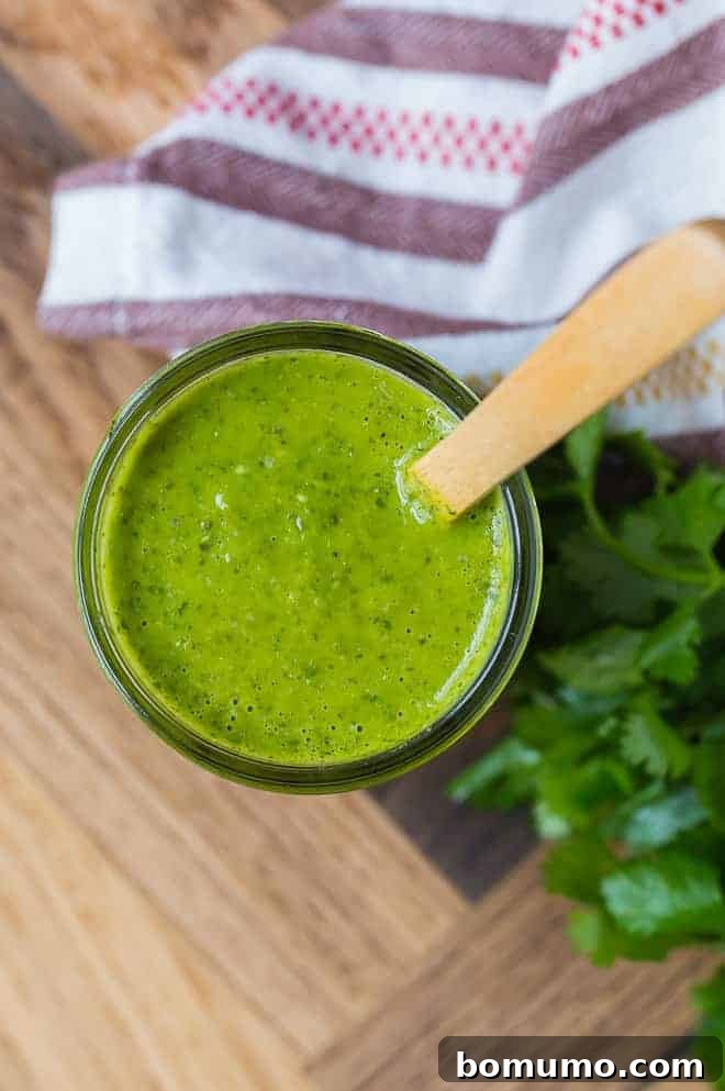 Image of a jar of freshly homemade salsa verde, shot from above, with a wooden spoon nestled inside.