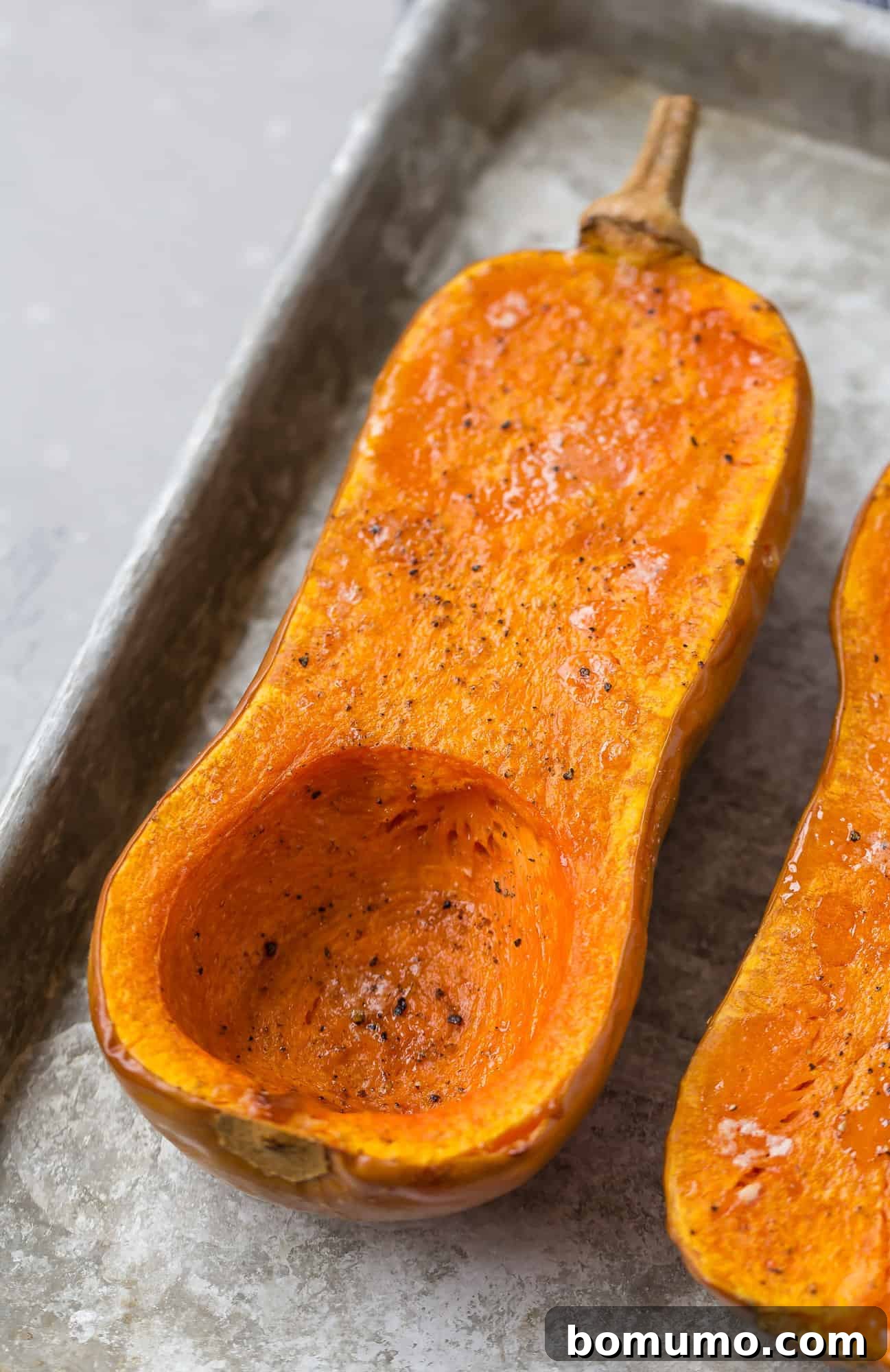 Two roasted butternut squash halves, golden brown and ready to be served or mashed, on a baking sheet.