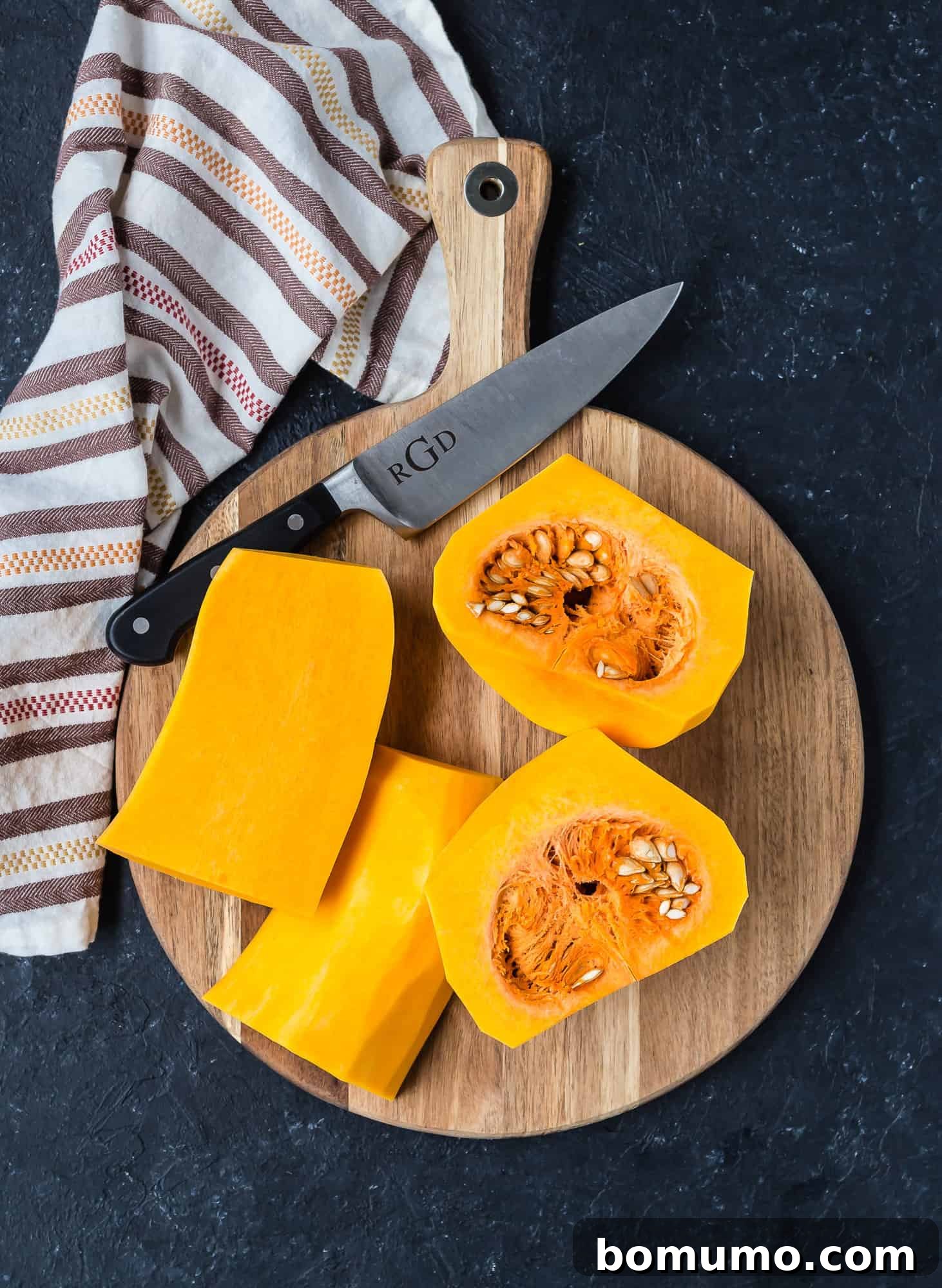 Peeled butternut squash, now cut into four quarters, laid on a cutting board.