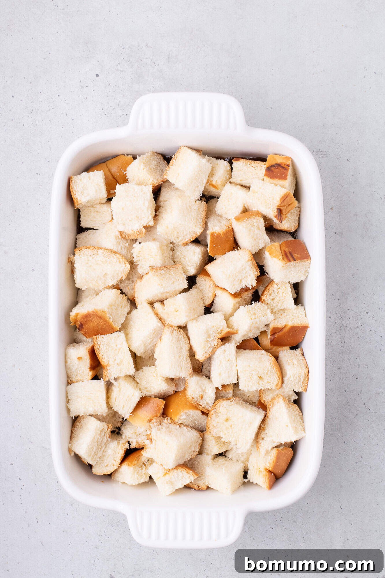 A white baking dish filled with evenly arranged bread cubes.