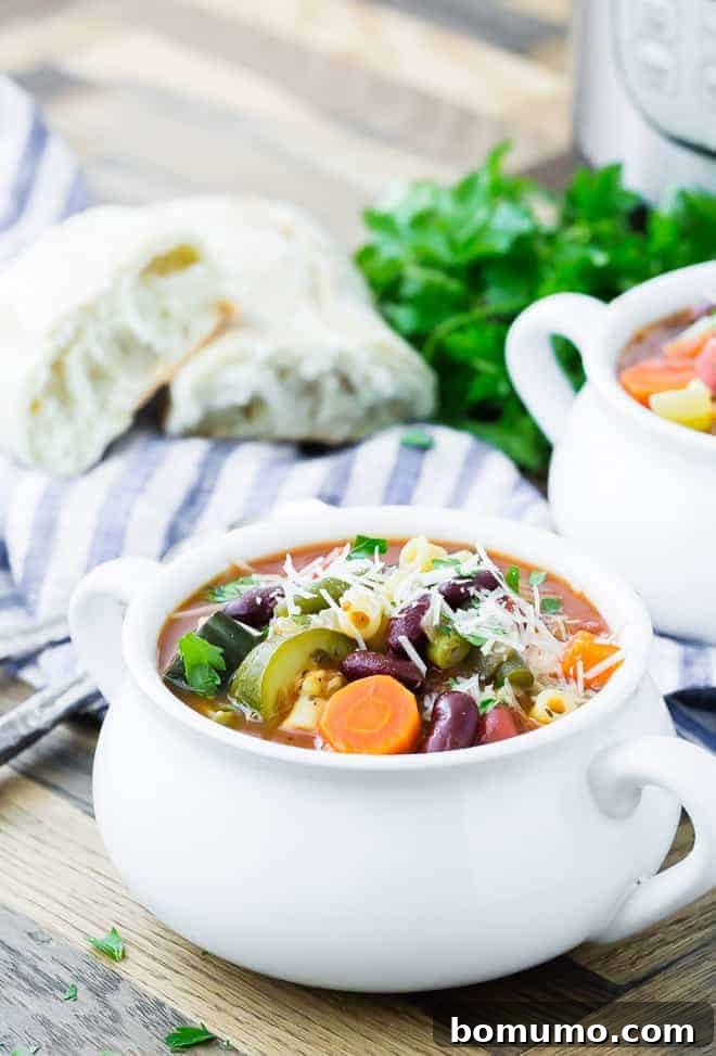 Image of pressure cooker minestrone in a bowl. Another bowl, parsley, bread, and an Instant Pot are in the background.