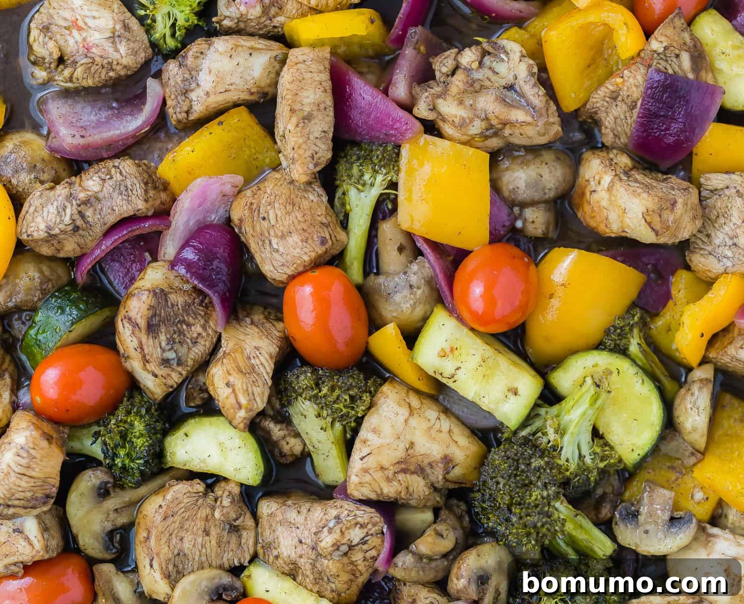 Close-up of roasted vegetables and honey balsamic chicken on a sheet pan.