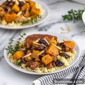 Two plates of chicken, couscous, squash, garnished with almonds.