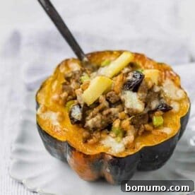 Stuffed acorn squash filled with farro, sausage, apples, and cheese on a white plate, with a fork stuck into the filling.