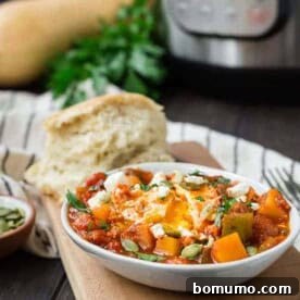 Small white oval bowl filled with tomato sauce, cubed squash, an egg, feta cheese, and pepitas.