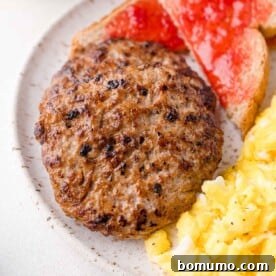 Two cooked sausage patties on a plate with scrambled eggs and toast topped with red jam.