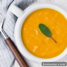 Squash soup in white bowl topped with sage.