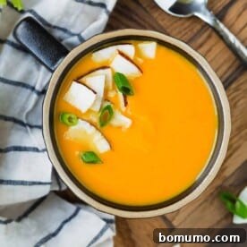 Overhead view of bright orange carrot soup with coconut and green onion garnish.
