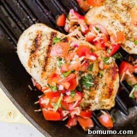 Image of bruschetta chicken with grill marks and bruschetta topping. Chicken is in a grill pan with two more chicken breasts.