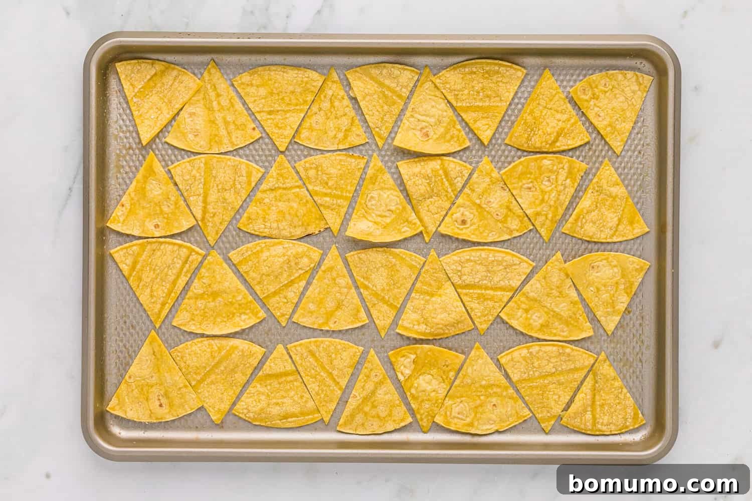 Corn-tortilla-chips-2 Unbaked corn tortilla wedges neatly arranged in a single layer on a baking sheet, ready for the oven.